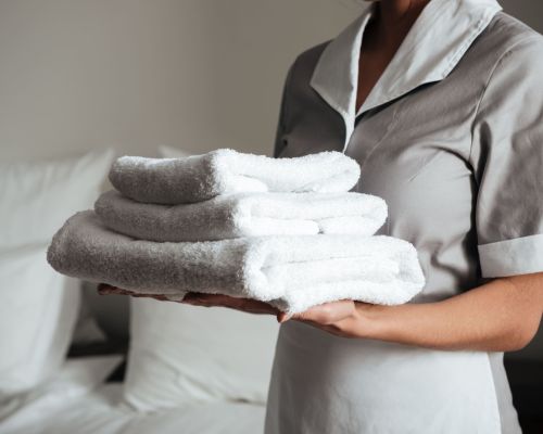 young-hotel-maid-standing-holding-fresh-clean-towels-min